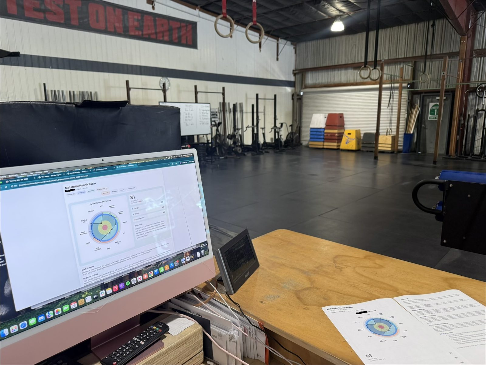 A Metabolic Radar report on a screen at the gym desk, with a printed report beside it and the empty gym floor behind.